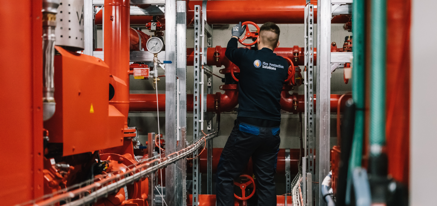 Techniker von Fire Protection Solutions führt Wartung an einer Brandschutzanlage mit roten Rohren und Ventilen durch