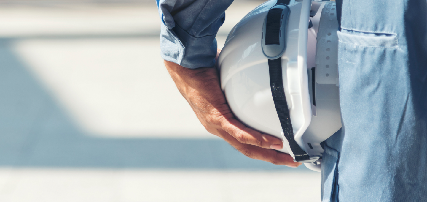 Person hält einen weißen Schutzhelm seitlich am Körper, Symbol für Arbeitssicherheit.