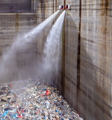 Zwei Löschmonitore sprühen Wasserstrahlen in ein großes Betonbecken mit Abfallmaterial